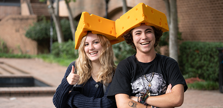 Two students smile forward, while wearing foam cheese hats.