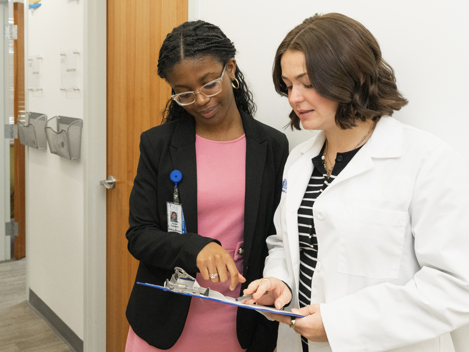 A student talks with a doctor as they examine a chart on a clipboard.