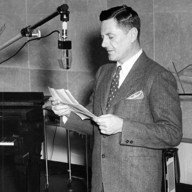 Burnet Maybank in a suit reading from papers into a studio microphone.