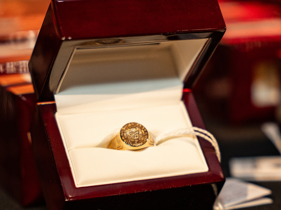 Gold College of Charleston class ring with an engraved round face displayed in an open, velvet-lined jewelry box.
