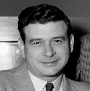 Black-and-white portrait of Frank Blair in a suit, with a hand resting on his shoulder.
