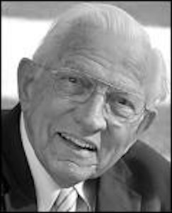 Close-up black-and-white portrait of James Edwards wearing glasses and a suit, smiling slightly.