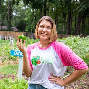 Smiling woman in a garden holding a green bell pepper.