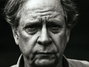 Black-and-white close-up portrait of Padgett Powell with a serious expression against a dark background.