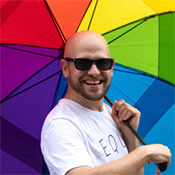 A smiling man holds an open rainbow pride umbrella behind him