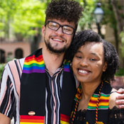 Two students pose for a photo wearing graduation pride stoles.