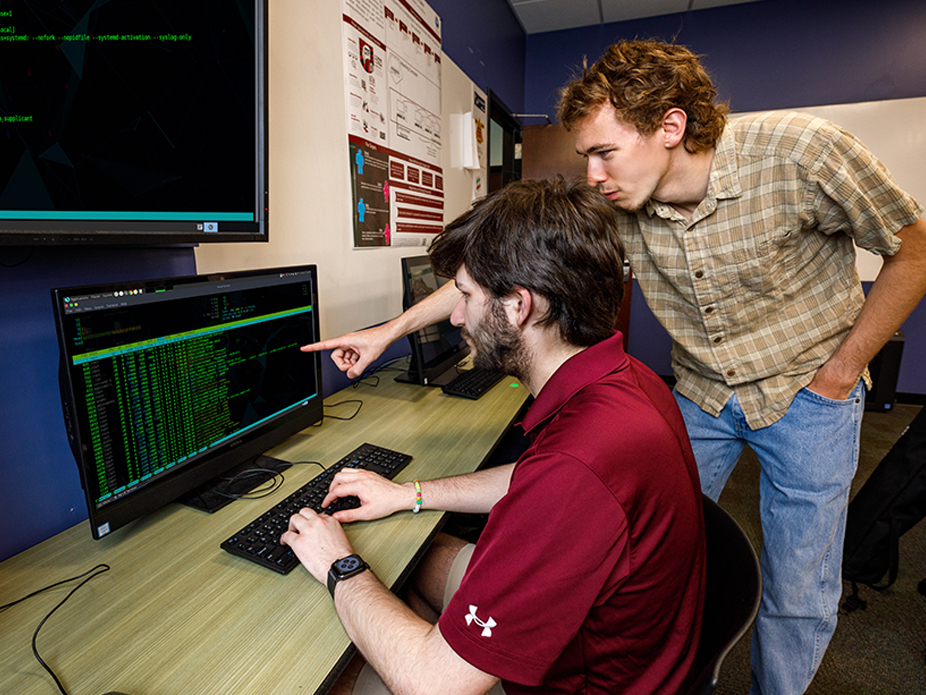 Two students examine a computer screen for cybersecurity issues.