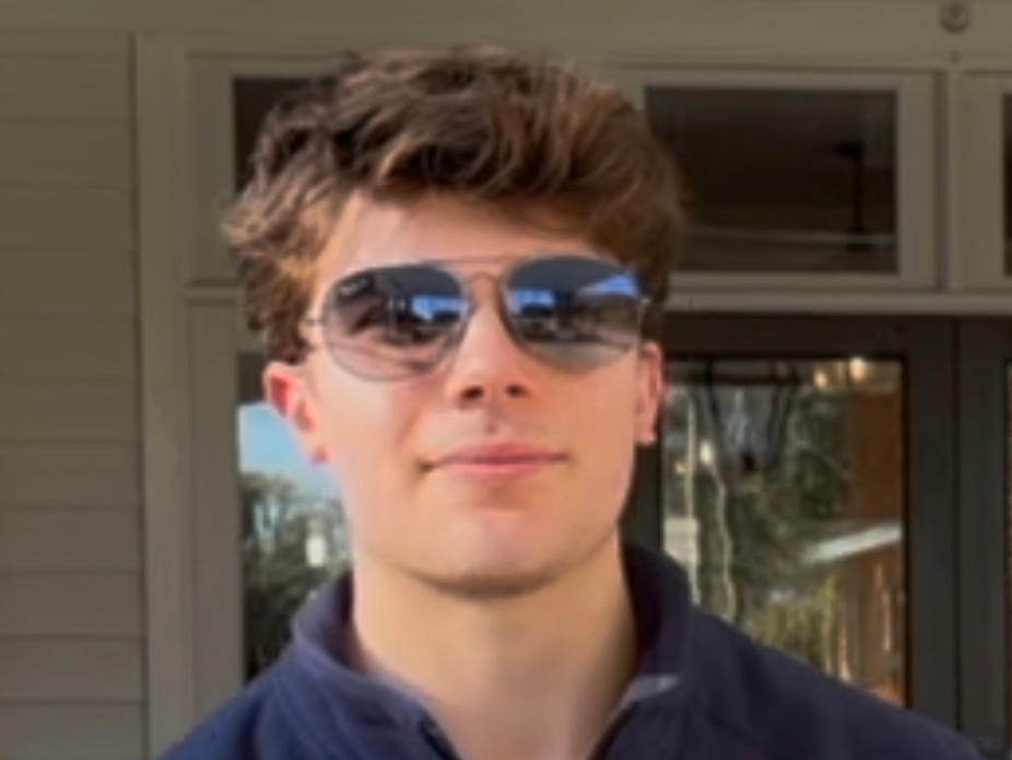 Image of a young man with shades smiling in front of windows