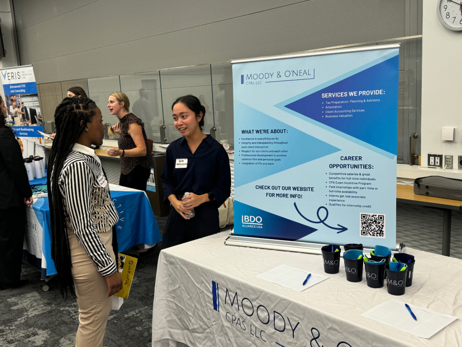 Two women in business casual clothing speaking to one another near a table