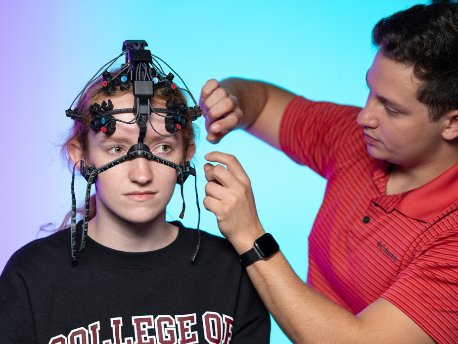 A male neuroscience researcher adjusts a headset on a female subject in a study to measure brain waves and music.