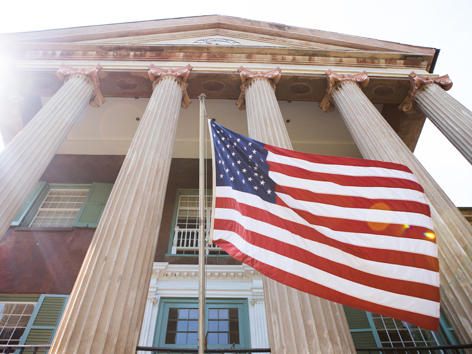 Steep angle looking up at the College of Charleston's iconic Randolph Hall  with the U.S. flag flying in the breeze.