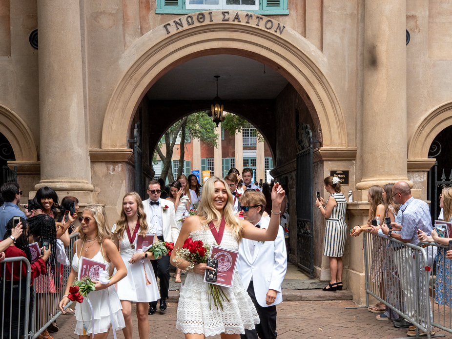 College of Charleston graduates dressed in their traditional white dresses and white dinner jackets, leave teh commencement ceremony under the arch at Porter's Lodge.