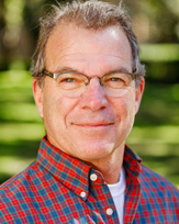 Bill Church, a smiling man in a plaid shirt with glasses, set against a blurred green background.