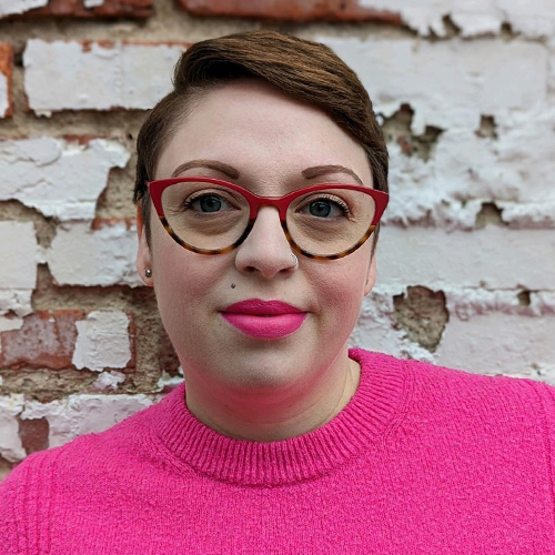 Head shot of Bex Farrell wearing cat-eye glasses and a pink sweater.