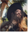 Portrait of a bearded man dressed as a pirate, wearing a large black hat and surrounded by palm trees.