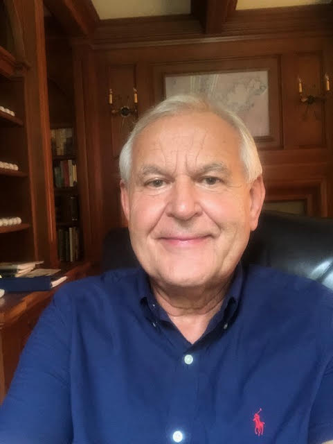 A smiling woman in a navy blouse standing by the water with a bridge in the background.