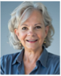 A smiling older woman with gray hair, wearing a light blue shirt and yellow earrings.