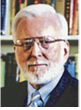 Portrait of a distinguished older man with glasses and white hair, dressed in a dark suit, against a backdrop of bookshelves.