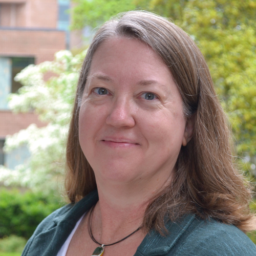 Portrait of Jennifer Kopfman with an outdoors background and a slight smile with shoulder length hair and teal jacket.