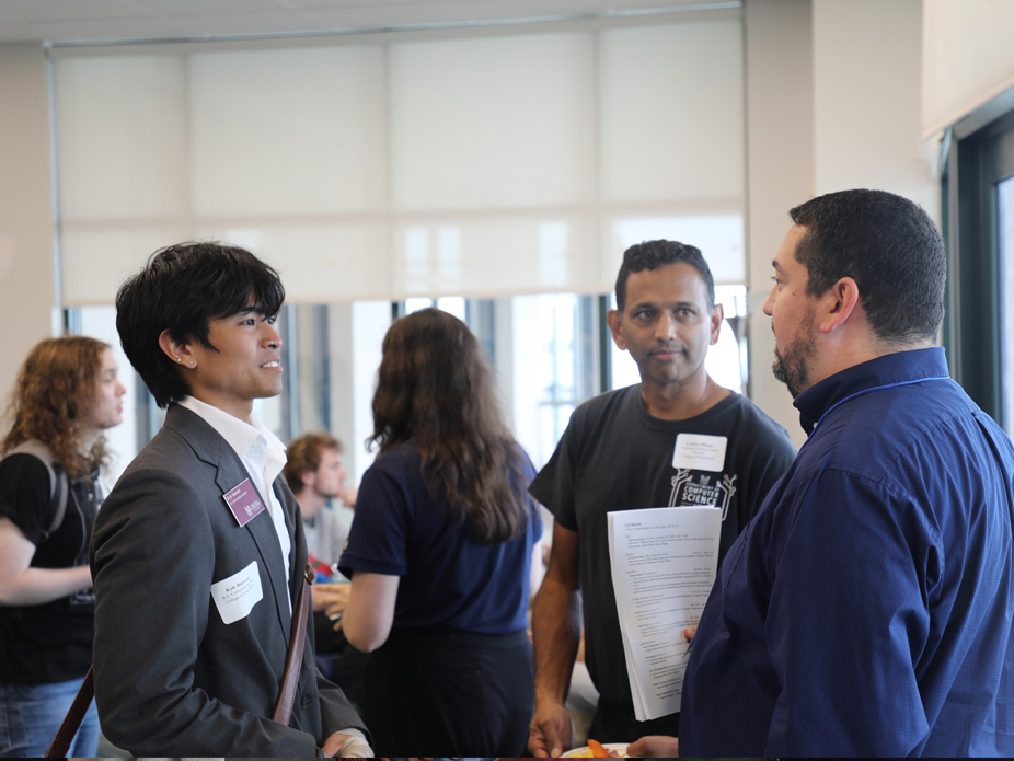 A male student in a sport coat speaks with a potential employer at BizBash