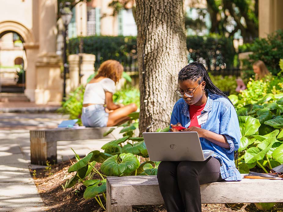 College of Charleston student sitting on a bench with a laptop. 