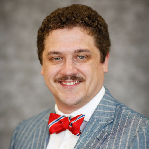A man in business professional attire smiling against a grey backdrop