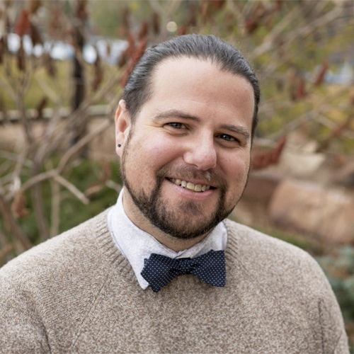Headshot of Matty Layne Glasgow, a smiling man with trimmed beard wearing a sweater and bow tie.