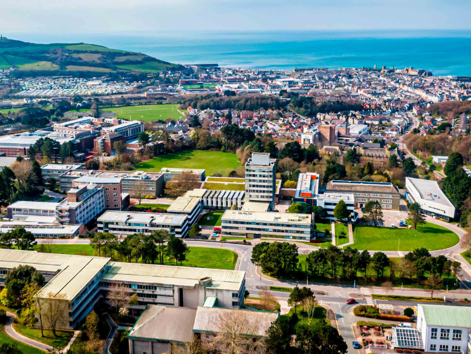 An aeiral view of the Welsh town of Aberystwyth, with city buildings offset along an ocean coastline.