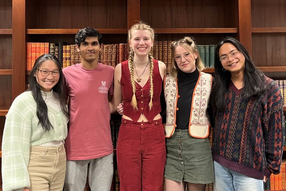 Students stand in front of a bookshelf with many fancy texts.