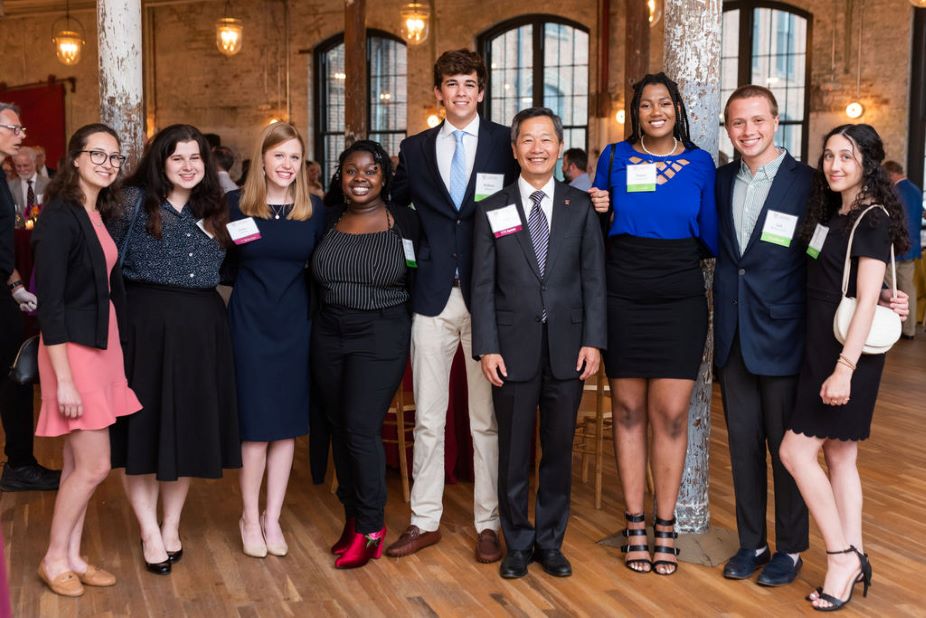 Students gather at a fancy donor reception and pose for the camera next to the College's president, Andrew Hsu.