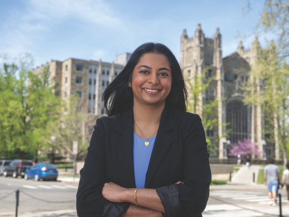 A young woman wearing a black blazer poses in front of an ornate building.