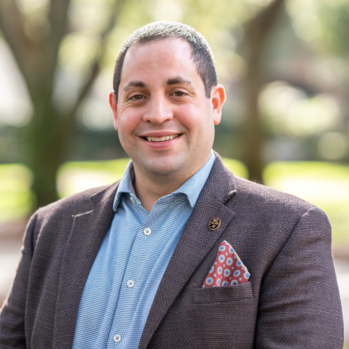A professional man smiling outside on a sunny day