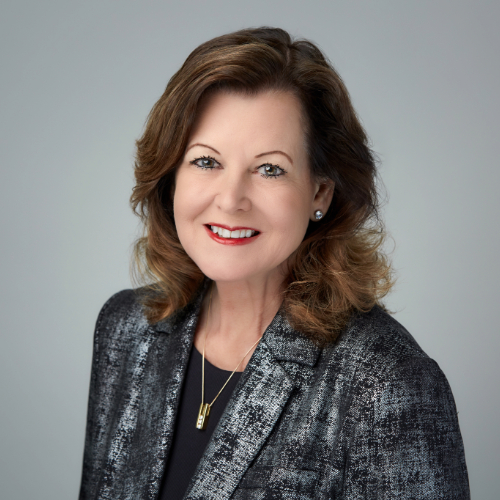 Professional headshot of a smiling woman with shoulder-length hair, wearing a black and silver jacket.