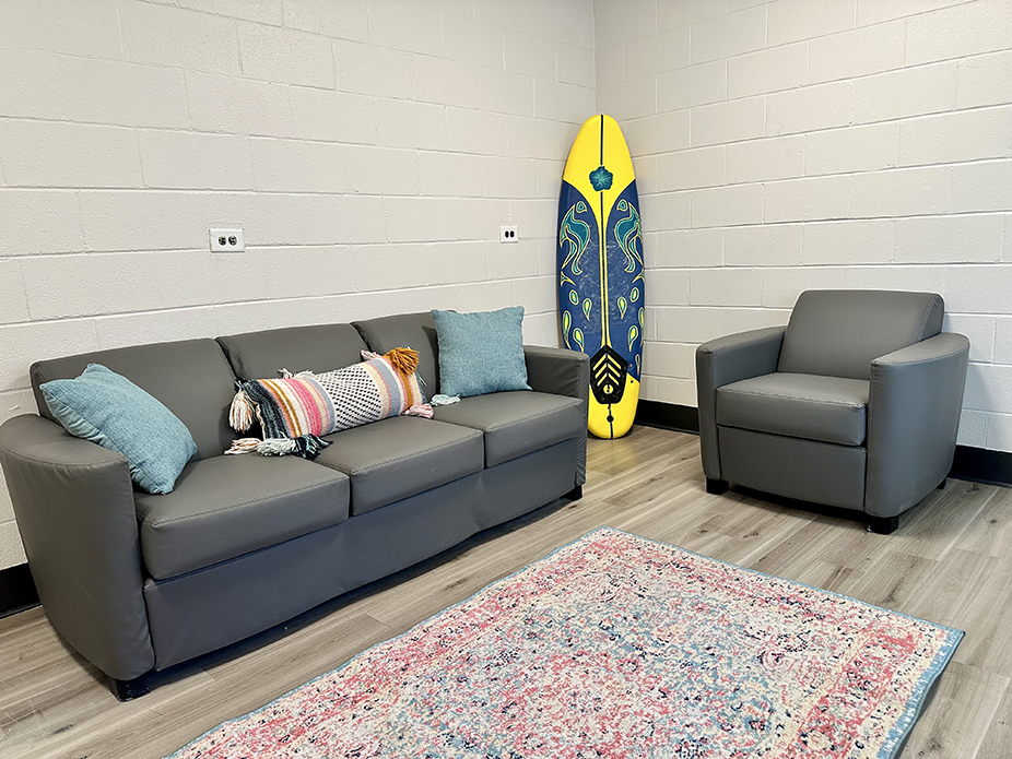 3-cushion sofa and chair in a rectangular common room. there is a surfboard in the corner of room.