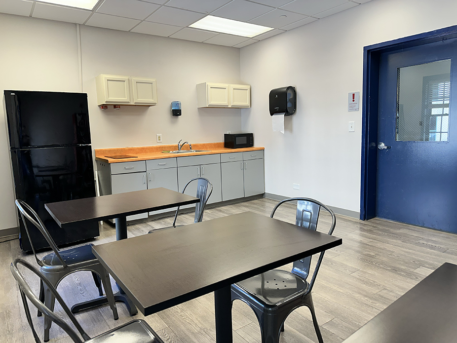 common kitchen in Craig Hall showing a full-size refrigerator, counter with two-burner stovetop, sink, microwave and two tables with two chairs each
