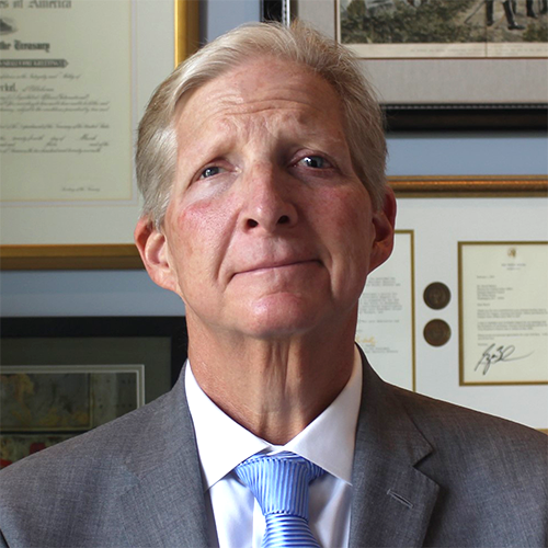 Portrait photograph of David Merkel, a Caucasian man, standing in front of a wall filled with framed certificates and paintings