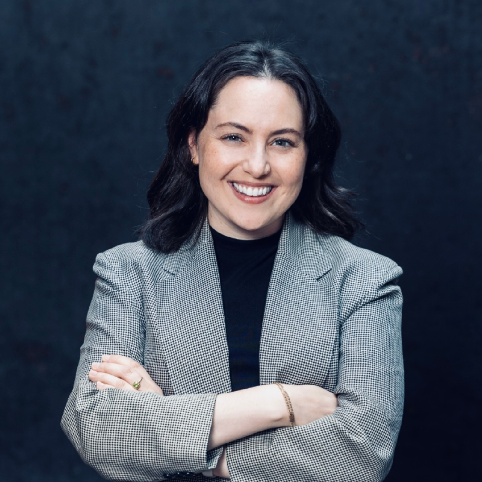 Hana Green smiling with her arms crossed in front of a blue background.