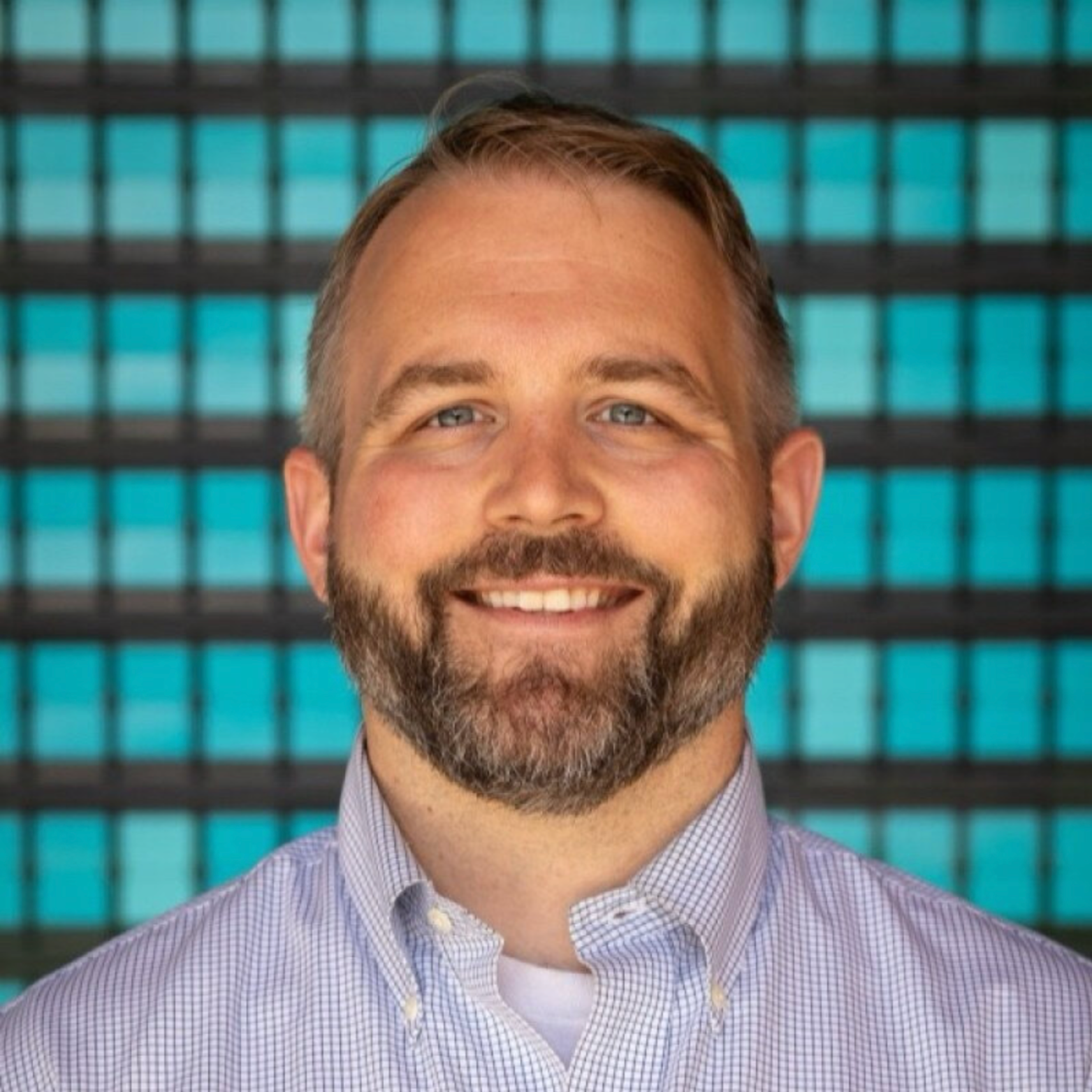 Time Cohen smiling in front of a pattern of blue squares.