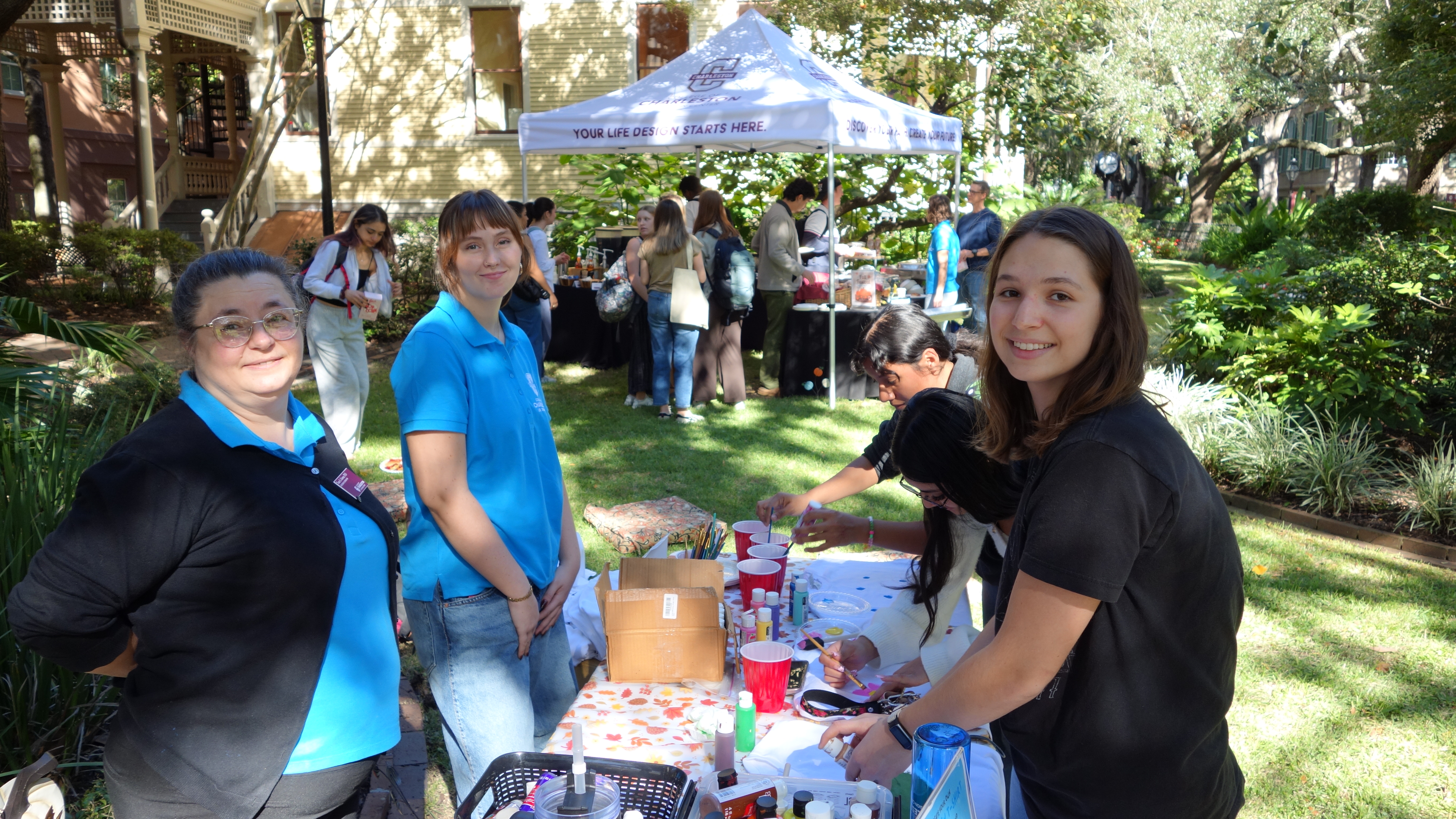 Students gather around a table painting designs onto plain white T-shirts at the Life Design T-shirt making station during Fall Fest.