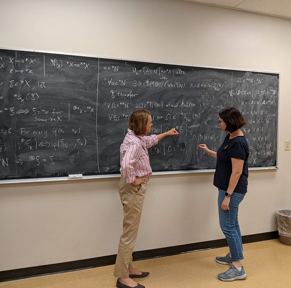 Student and faculty member discuss problem in front of chalk board