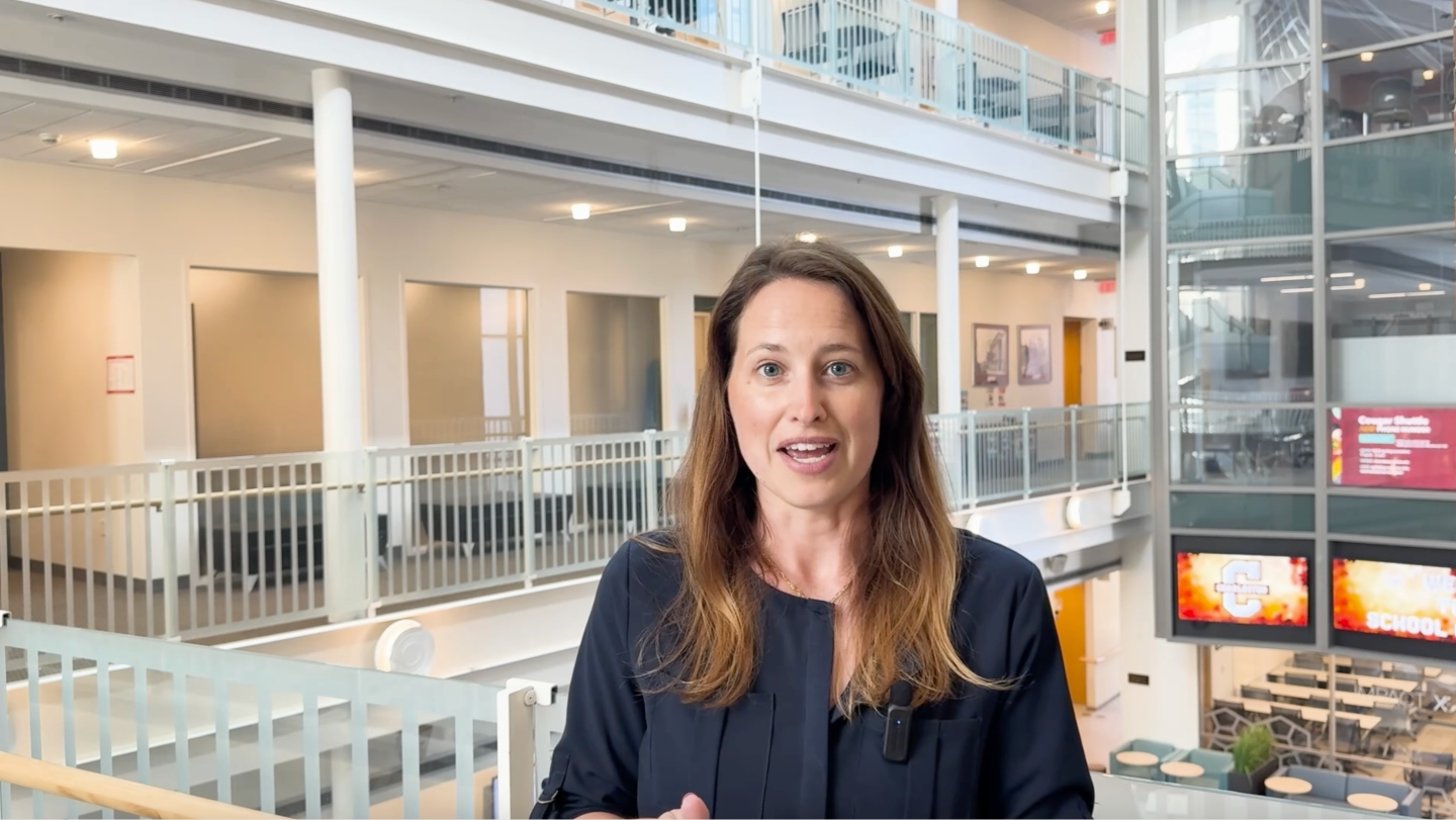 A woman in a dark shirt speaking to the camera