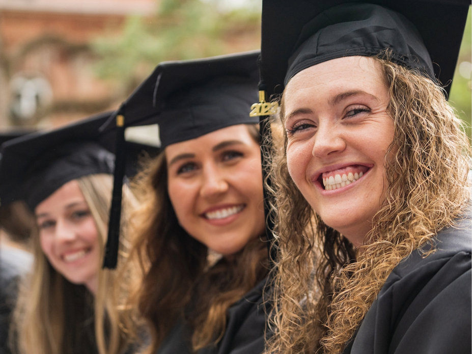 Three women smiling at graduating with black cap and gowns on