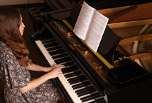 A woman playing piano with sheet music displayed on the stand.