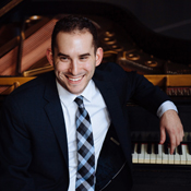 Mackenzie Melemed, a smiling man in a suit leaning on a grand piano keyboard.