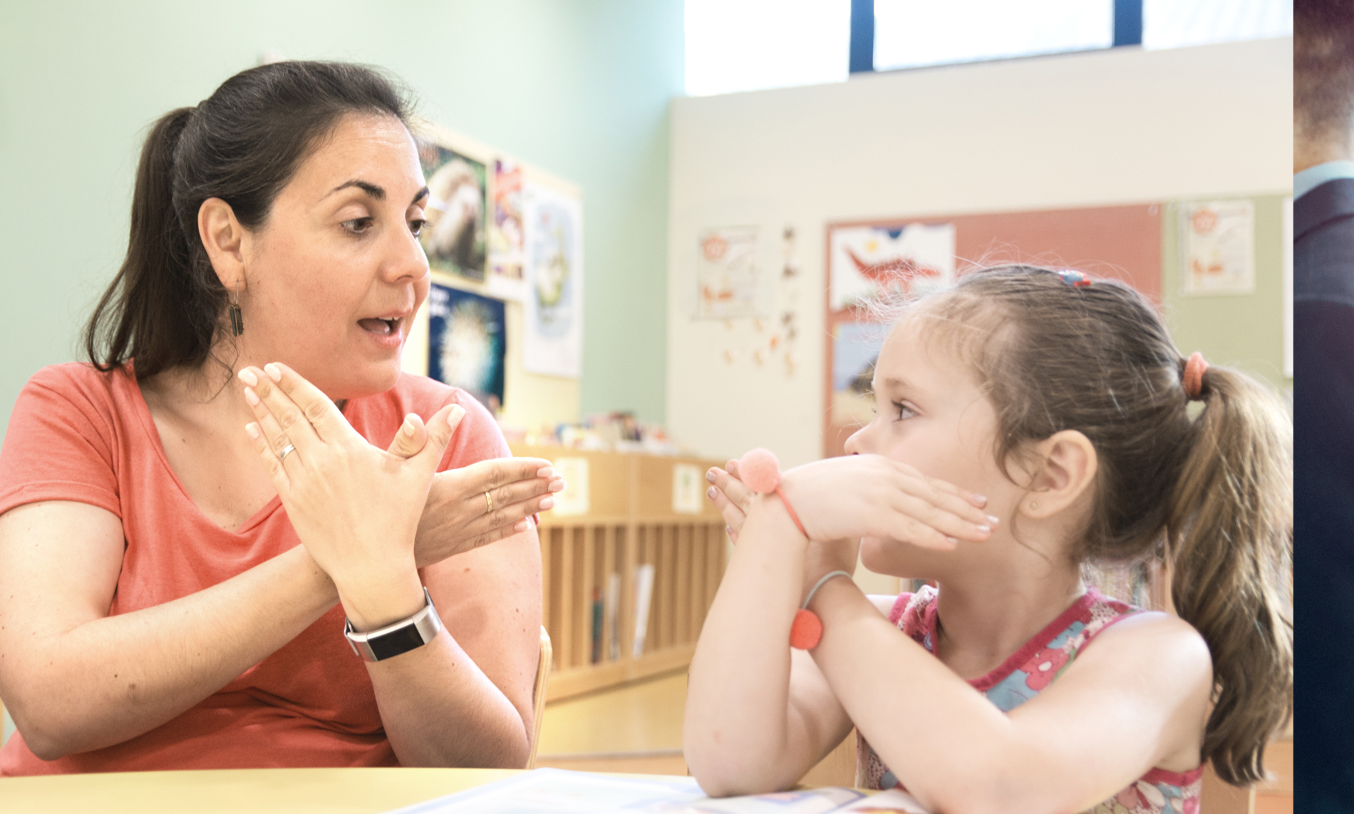 Teacher and young student practicing sign language together in a classroom.