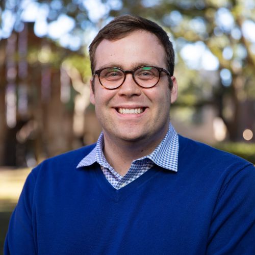 Professional portrait of Patrick Ramsay, a smiling man with short brown hair and glasses in an outdoor setting.