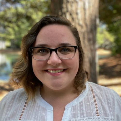 Professional portrait of Kelsey Vollmer, a smiling woman with short brown hair and glasses in an outdoor setting.