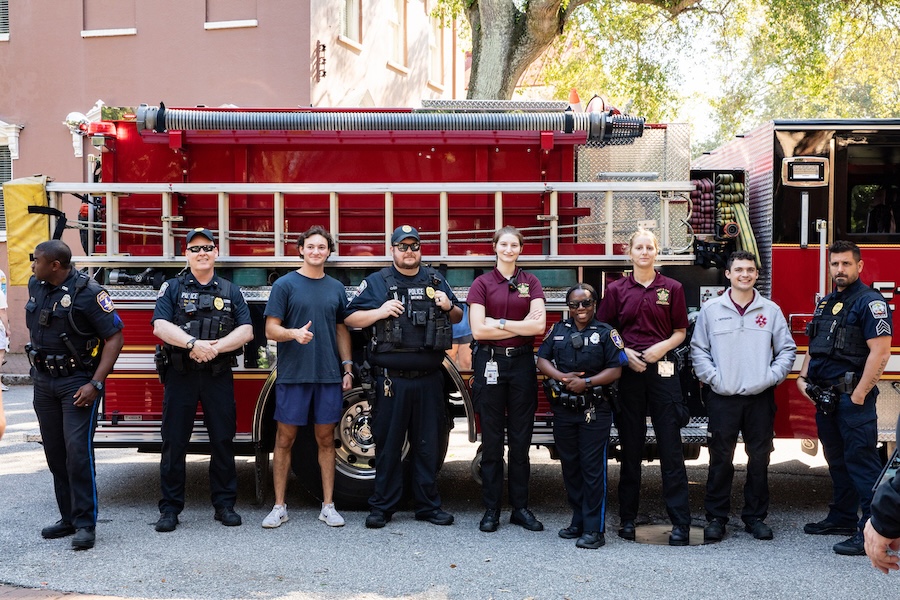 Group of police officers and emergency responders standing in front of a red fire truck outdoors.