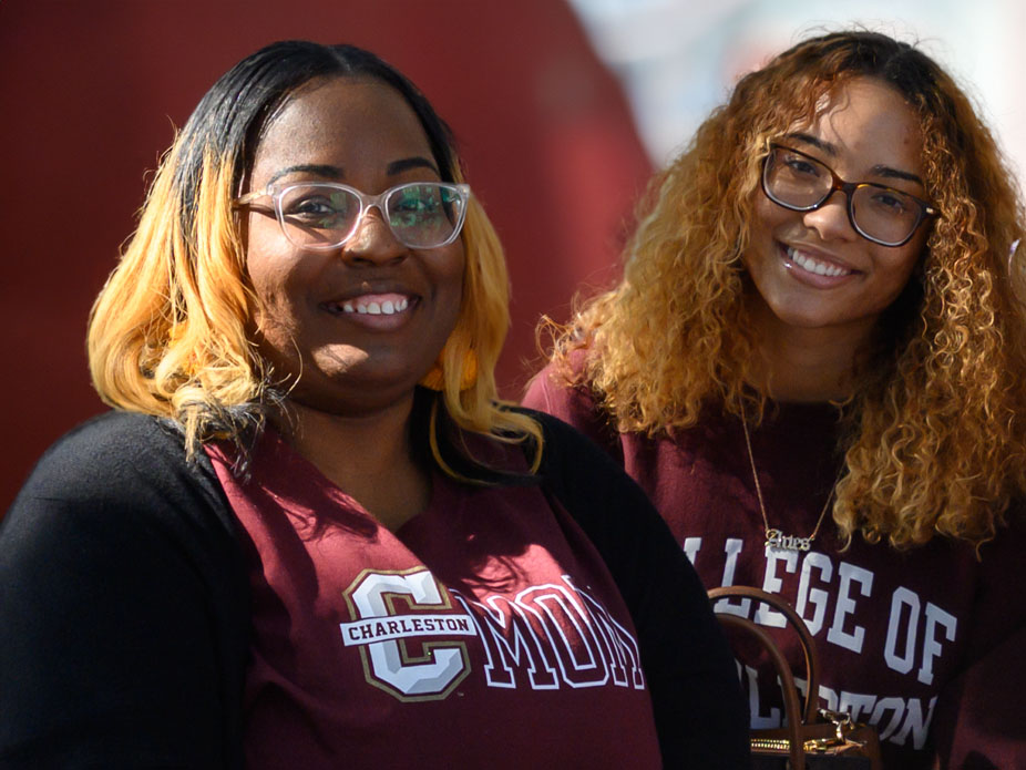 An Africa-American Charleston mom and student wearing College of Charleston gear smile for the camera.