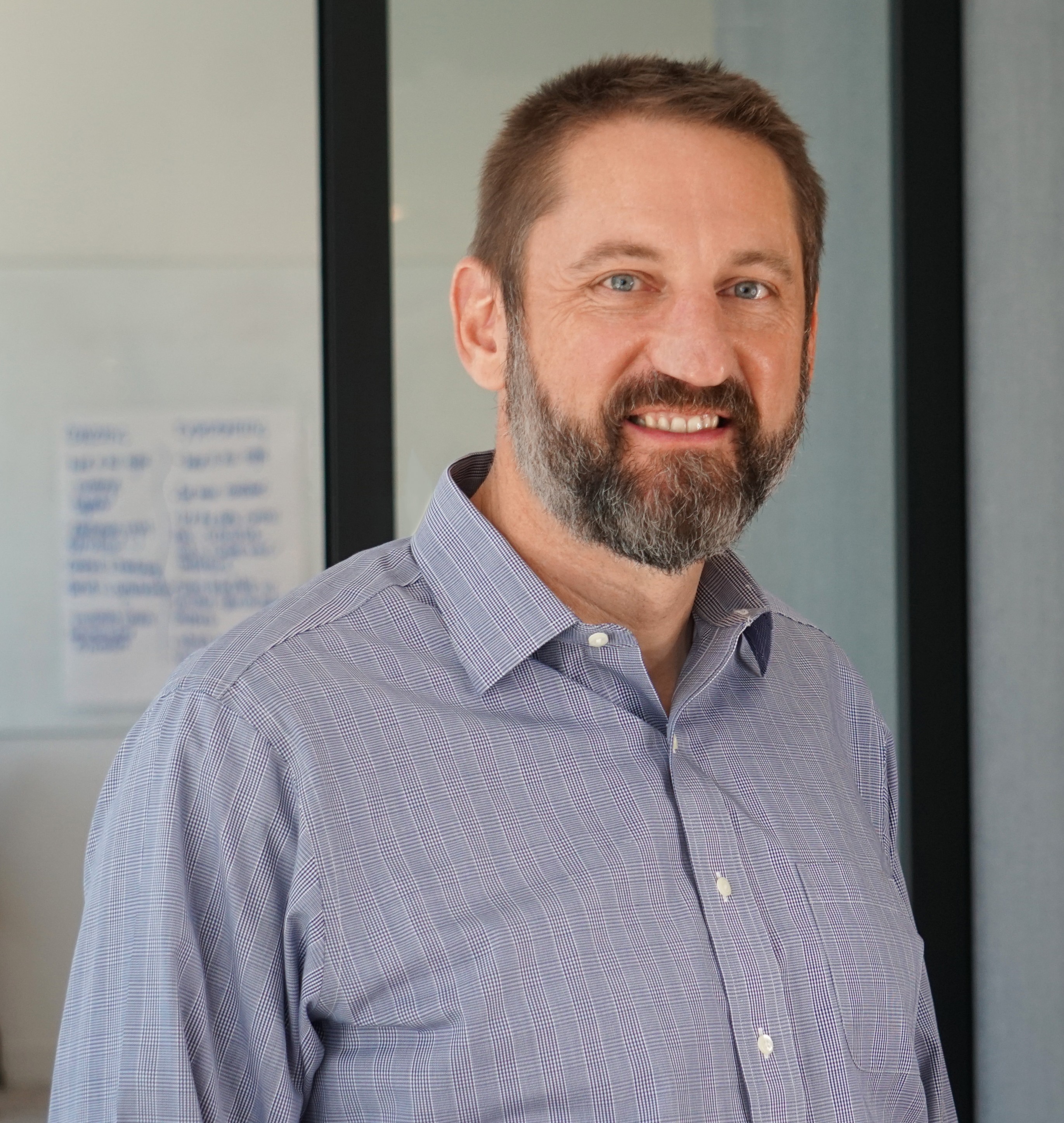 Man with brown hair and graying beard wearing a blue button up shirt